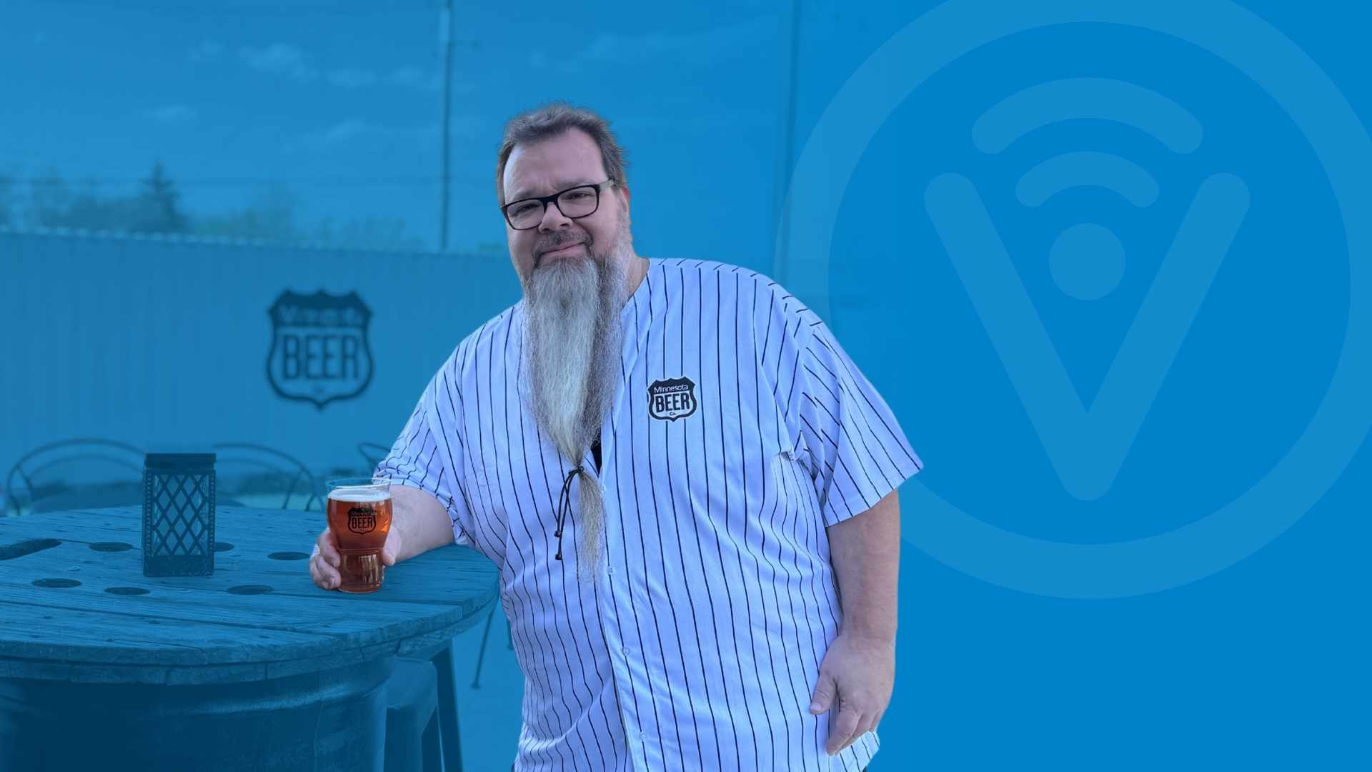 Person looking at camera holding a beer and leaning on a table.